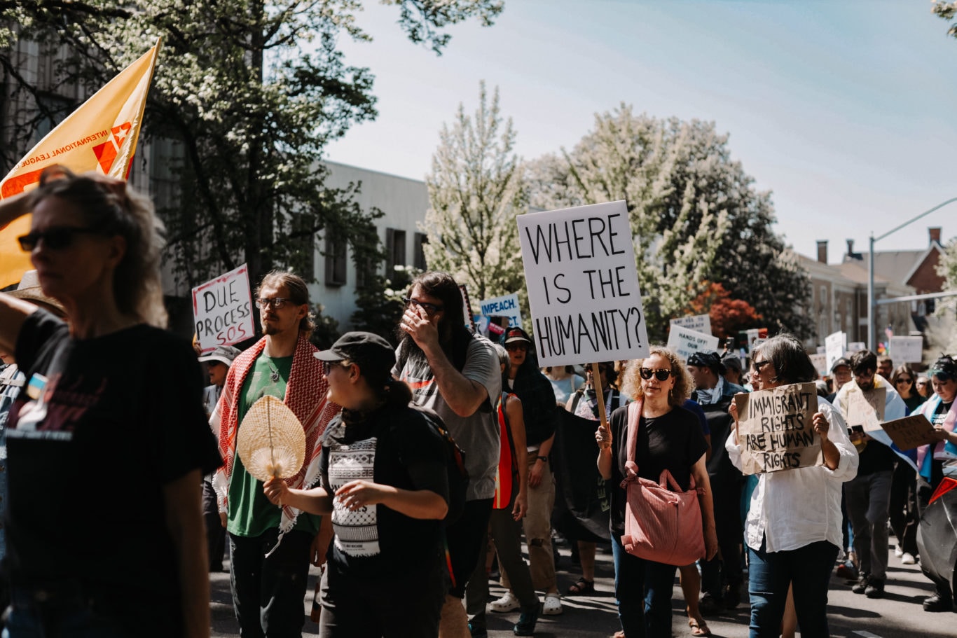 Crowd of Oregonians protesting the cuts from the federal government and a person carrying a sign that says "where is the humanity?"