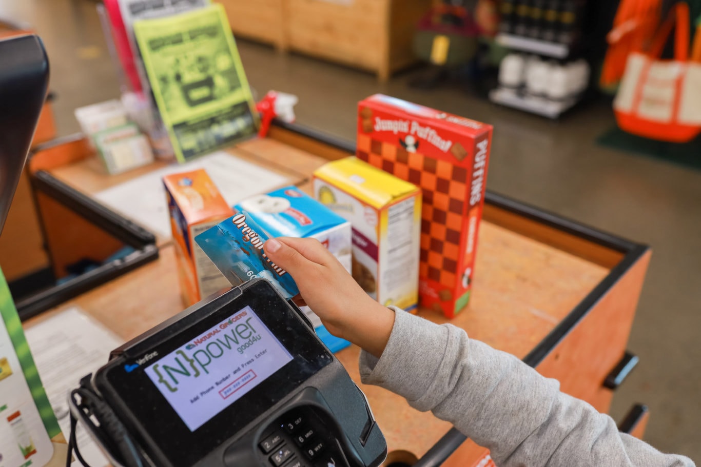 A person uses an Oregon Trail EBT card to buy groceries at a checkout counter.